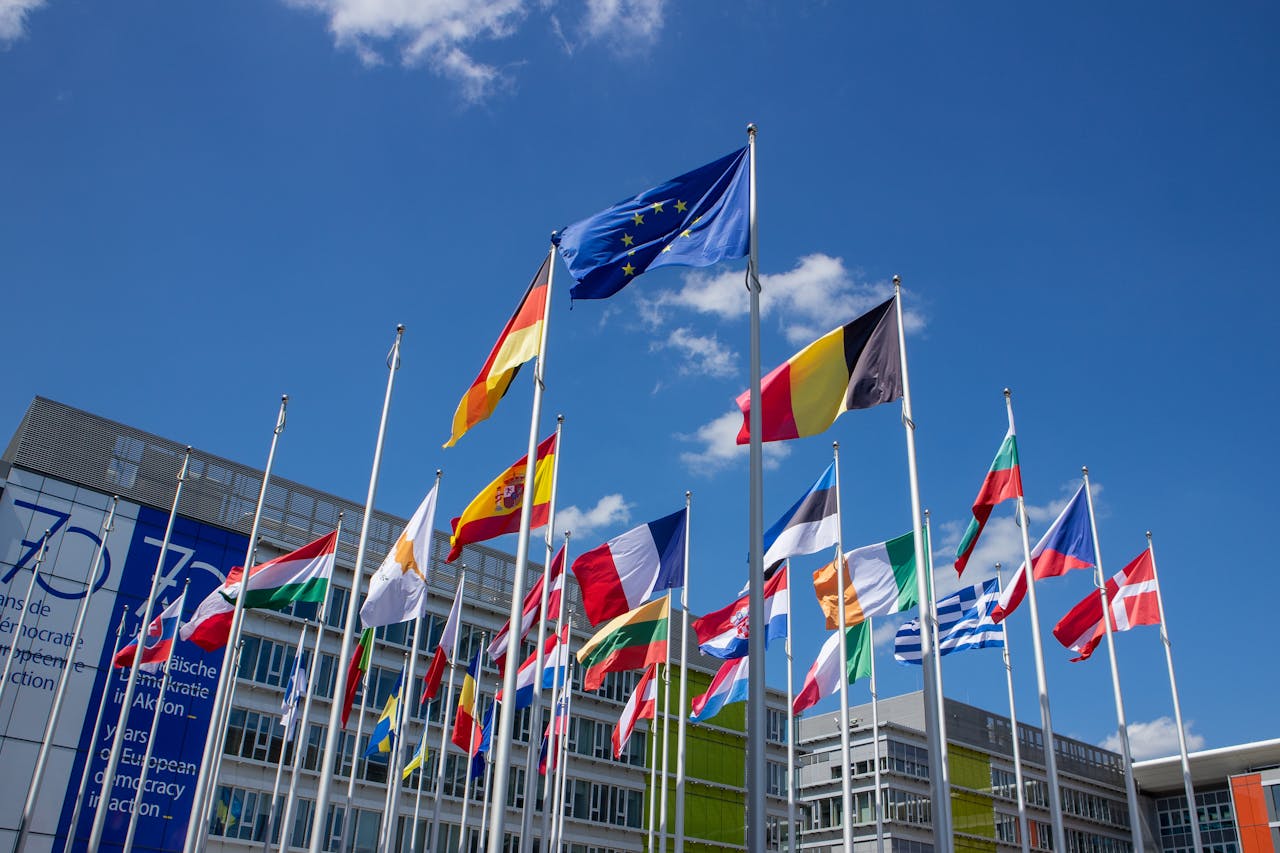 Low angle view of European Union flags on flagpoles against a blue sky, symbolizing unity.